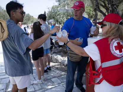 أعضاء من الصليب الأحمر الهيليني يوزعون زجاجات مياه على سياح عند مدخل موقع الأكروبوليس الأثري، وسط موجة حر شديد، في أثينا ، اليونان ، يوم الجمعة  14 يوليو 2023 - المصدر: بلومبرغ