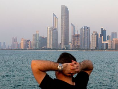 شخص ينظر إلى أفق مدينة أبوظبي من ضفة كورنيش المدينة، وتظهر في العمق أبراج الأعمال في العاصمة الإماراتية. أبوظبي، الإمارات العربية المتحدة. - المصدر: بلومبرغ