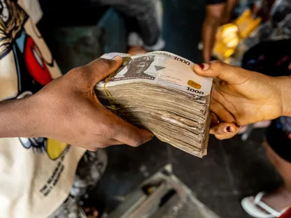أحد العملاء يسلم حزماً من أوراق نقدية فئة 1000 نيرة لتاجر داخل سوق بمدينة لاغوس في نيجيريا. الجمعة 22 أبريل 2022 - المصدر: بلومبرغ