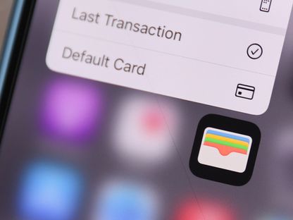 شاشة هاتف ذكي تظهر عليها أيقونة تطبيق المحافظ الرقمية (Apple Wallet)، مع جزء من القائمة الخاصة بالتطبيق والتي تشمل خيارات مثل \"أحدث عملية\" و\"البطاقة الافتراضية\" - المصدر: بلومبرغ