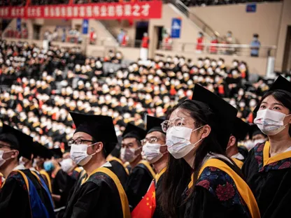 طلاب صينيون من جامعة \"هواتشونغ\" للعلوم والتقنية يتابعون فيلماً قصيراً على شاشة عرض ضخمة خلال احتفال التخرج بصالة للألعاب الرياضية بالكلية - المصدر: بلومبرغ