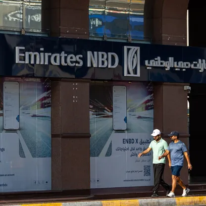 شخصان يمران أمام فرع لبنك الإمارات دبي الوطني في أبوظبي، الإمارات. البنك المملوك جزئياً من قبل حكومة دبي يعيّن بنوكاً لترتيب اجتماعات مع مستثمرين لمناقشة إصدار سندات مقومة بالدولار. - بلومبرغ