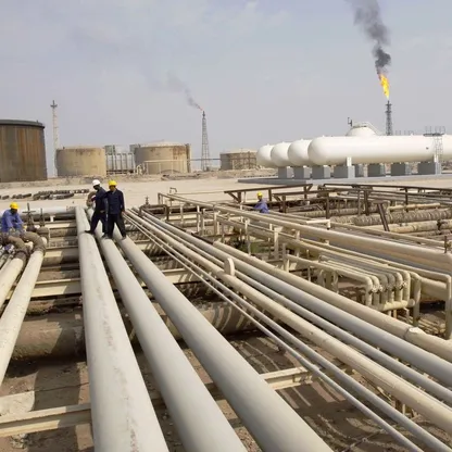 عمال عراقيون يسيرون على خطوط أنابيب في مصفاة نفط بالقرب من مدينة البصرة - المصدر: بلومبرغ