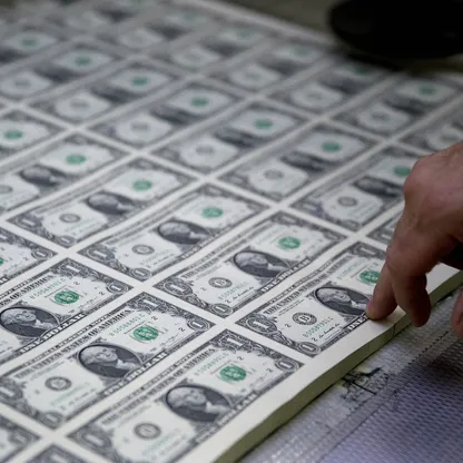 شخص يشير بإصبعه إلى ورقة نقدية فئة 1 دولار ضمن رزم من العملة الأميركية - بلومبرغ