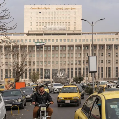 صورة من وسط العاصمة السورية دمشق تظهر سيارات وفي الخلف مقر مصرف سورية المركزي وعليه العلم الجديد للبلاد - بلومبرغ