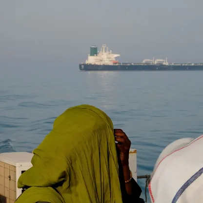 امرأة على قارب يحمل علم إيران تنظر إلى ناقلة نفط في مضيق هرمز - بلومبرغ
