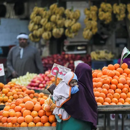 سيدة تحمل رضيعاً تشتري فاكهة من إحدى الأسواق في مصر. - المصدر: بلومبرغ