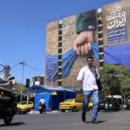 أشخاص يعبرون شارعاً قرب لوحة إعلانية تصور مضيق هرمز وعليها عبارة بالفارسية تقول "إلى الأبد في يد إيران"، في ساحة ونك بطهران في 25 مايو - بلومبرغ