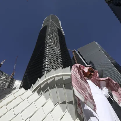 رجل بالزي الوطني السعودي يعبر من أمام برج في مركز الملك عبدالله المالي في العاصمة الرياض - المصدر: بلومبرغ