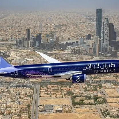 طائرة تحمل شعار "طيران الرياض" تحلق بسماء العاصمة السعودية، ويبدو بالأفق مركز الملك عبدالله المالي - المصدر: بلومبرغ