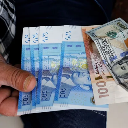 رجل يعرض أوراقاً نقدية من فئات 100 و200 درهم مغربي و100 دولار - المصدر: بلومبرغ