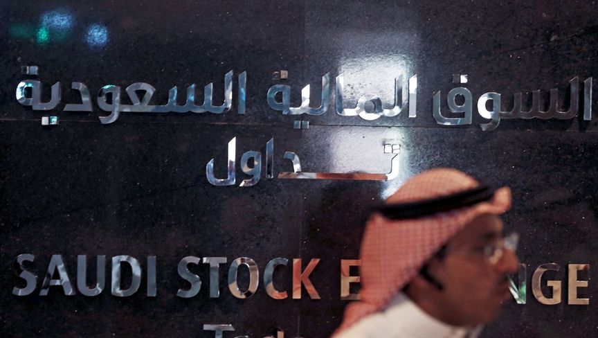 رجل يعبر من أمام جدار تزين بشعار السوق المالية السعودية "تداول"، داخل مقر البورصة في العاصمة السعودية الرياض (15 يونيو 2015) - المصدر: بلومبرغ
