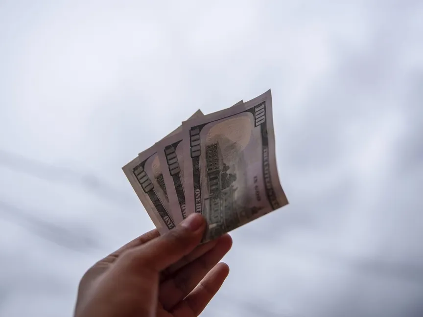 شخص يرفع في يده عملات ورقية من فئة 100 دولار أميركي. لا يزال المراهنون على هبوط الدولار تحت رحمة تطورات الوضع في إيران. - المصدر: بلومبرغ