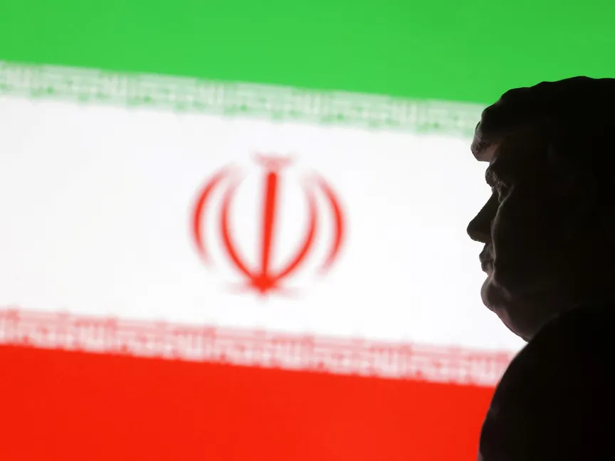 صورة تُظهر مواجهة رمزية بين إيران والولايات المتحدة، مع علم إيران في الخلفية، وظل شخصية تمثل الرئيس الأميركي دونالد ترمب - رويترز 