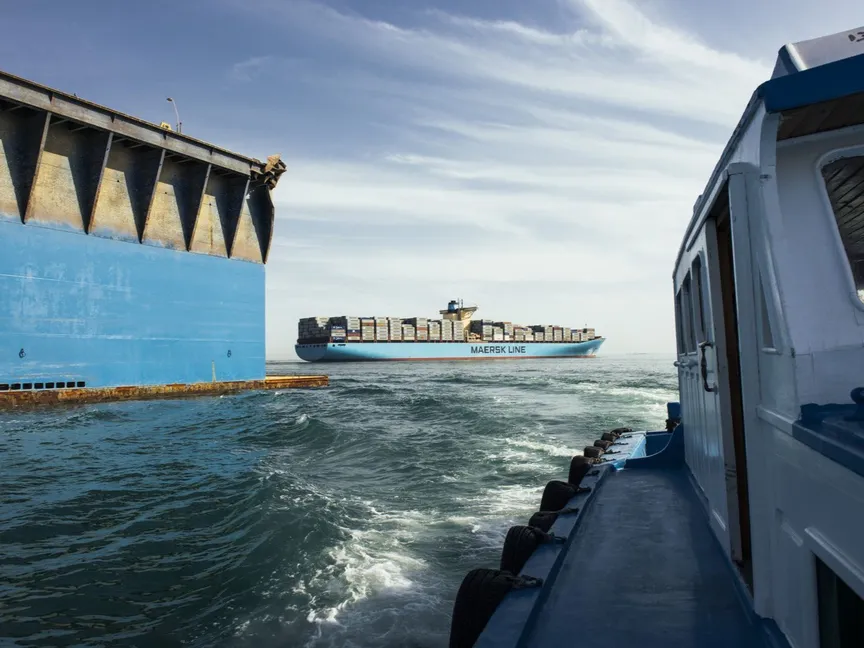 تتجه سفينة إرشاد تابعة لهيئة قناة السويس إلى الشاطئ بعد مغادرة سفينة الحاويات "إيبا ميرسك" تشغلها شركة "إيه. بي. مولر-ميرسك"، وسط الصورة، بينما تواصل مرورها عبر البحر الأحمر بعد خروجها من قناة السويس بمدينة السويس في مصر بتاريخ 6 أبريل 2013 - المصدر: بلومبرغ