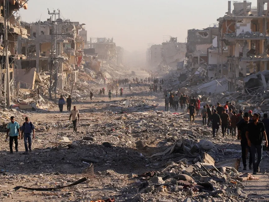فلسطينيون يسيرون عبر حي مدمر في مدينة غزة، بعد أن صادقت الحكومة الإسرائيلية على وقف إطلاق النار مع "حماس"، غزة، 10 أكتوبر 2025 - رويترز 