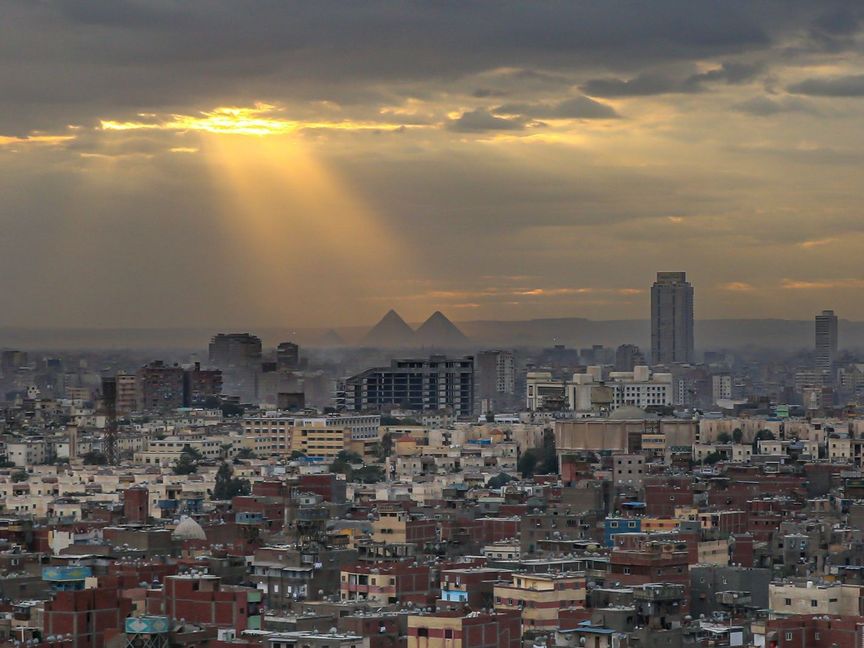 صورة تظهر مباني سكنية وتجارية في مدينة القاهرة، وفي الخلفية أهرامات الجيزة، مصر - المصدر: بلومبرغ