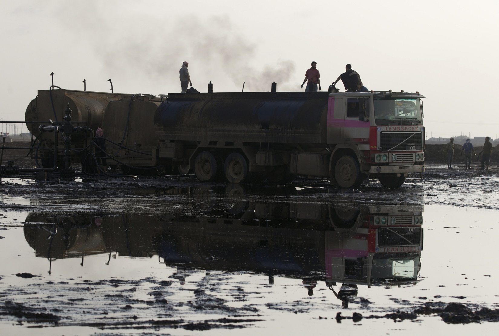 أشخاص يعتلون ظهر شاحنة لنقل الوقود في منطقة ملوثة بالنفط الخام بالقرب من حقل الرميلان، القامشلي، سوريا، 11 نوفمبر 2013.