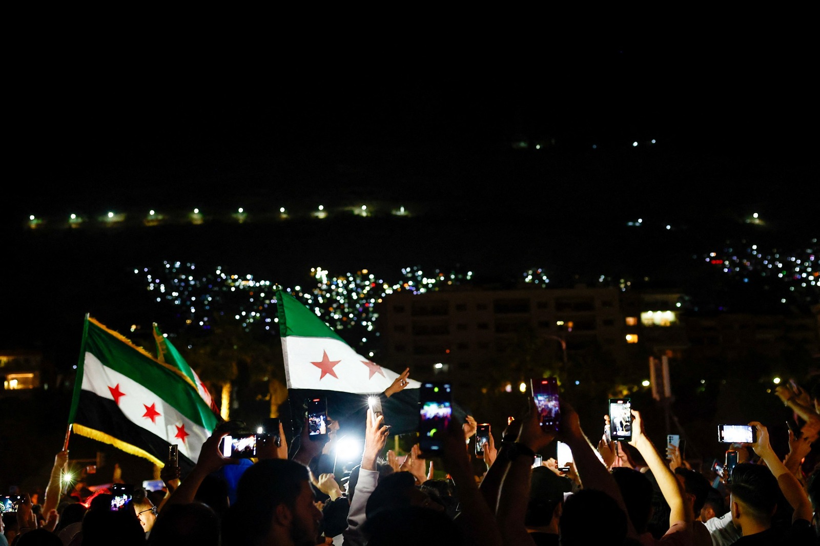مواطنون سوريون يحتفلون على ضوء هواتفهم بقرار الرئيس الأميركي دونالد ترمب برفع العقوبات عن بلادهم، دمشق، 13 مايو 2025. - رويترز